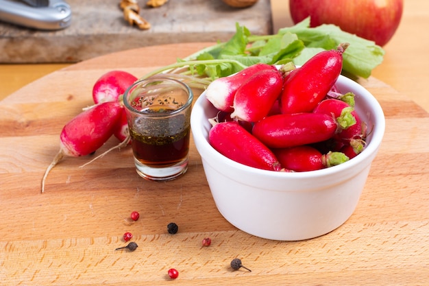 Alimento che prepara ravanello oraganic dentro con la tazza con l&#39;insalata e le spezie di condimento sul bordo di legno