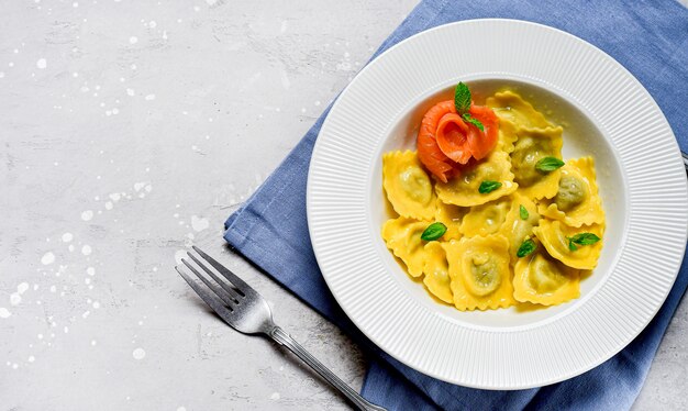 Alimento italiano tradizionale dei ravioli di color salmone con basilico fresco in un piatto bianco su una tavola di pietra grigia. Ricetta cibo italiano. cibo piatto disteso