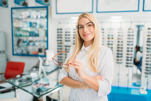 All'ottico optometrista femmina tiene gli occhiali in mano, vetrina con gli occhiali nel negozio di ottica. Selezione di occhiali da vista con ottico professionista