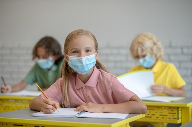 Alla lezione. Ragazza in maschera seduto alla lezione e guardando concentrato