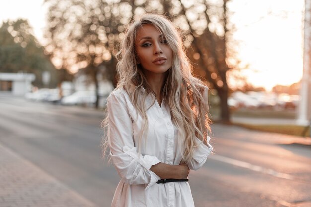 Alla moda bella donna modello elegante con trucco naturale cammina per strada in città al tramonto