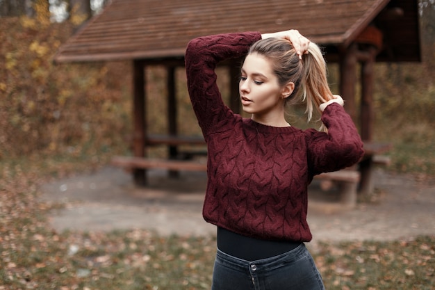 Alla moda bella giovane donna in un elegante maglione lavorato a maglia vintage vicino a una casa in legno in natura