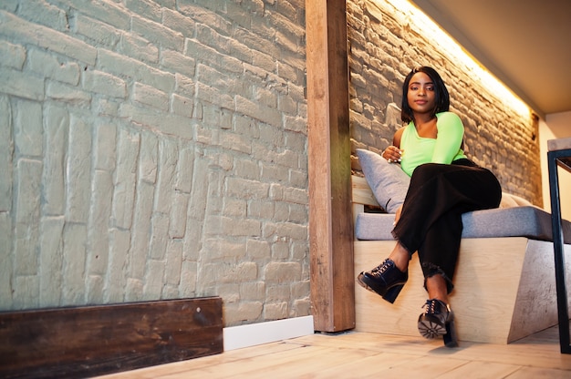 Alla moda donna afroamericana in un top verde chiaro e pantaloni neri pongono.