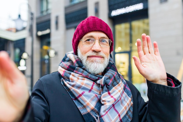 Alla moda vecchio bell'uomo che fa selfie in sity street in inverno vicino a un edificio moderno