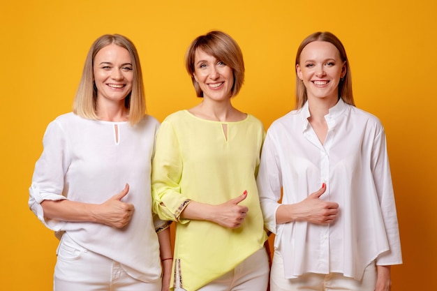 Alle donne soddisfatte piace il ritratto di gruppo di incoraggiamento del supporto del segno di approvazione del gesto di tre donne felici