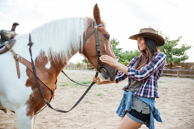 Allegra affascinante giovane donna cowgirl con cavallo in piedi e ridendo