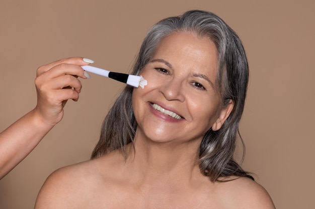 Allegra anziana signora caucasica gode di un trattamento antietà il cosmetologo applica la maschera crema con