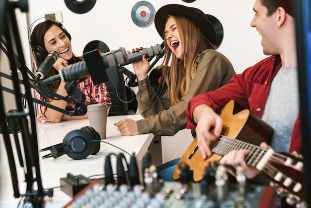 Allegra banda di giovani musicisti che suonano la loro canzone nella sala radio con un conduttore radiofonico, trasmissione radiofonica