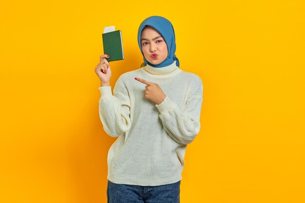 Allegra bella donna asiatica in maglione bianco che punta il passaporto con il dito isolato su sfondo giallo Summer Trip