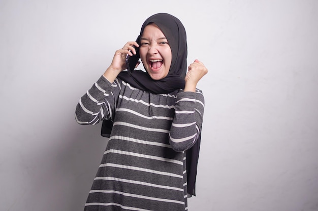 Allegra bella donna musulmana asiatica in maglione bianco e nero che parla al cellulare mentre si rallegra fortuna isolata su sfondo bianco Concetto di stile di vita religioso della gente