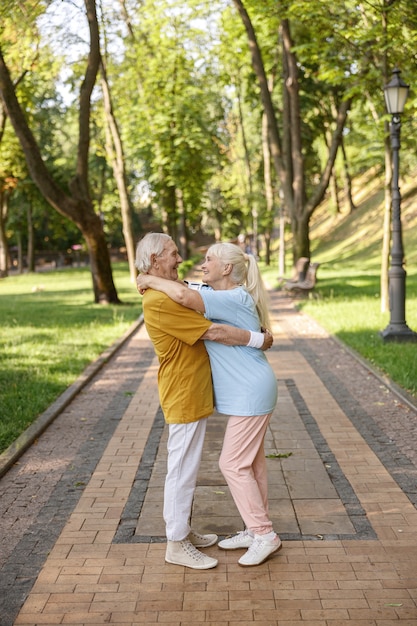 Allegra coppia senior in abiti sportivi abbracci in piedi sulla strada nel parco verde