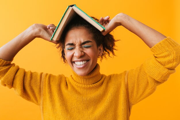 Allegra donna africana che indossa un maglione in possesso di un libro isolato