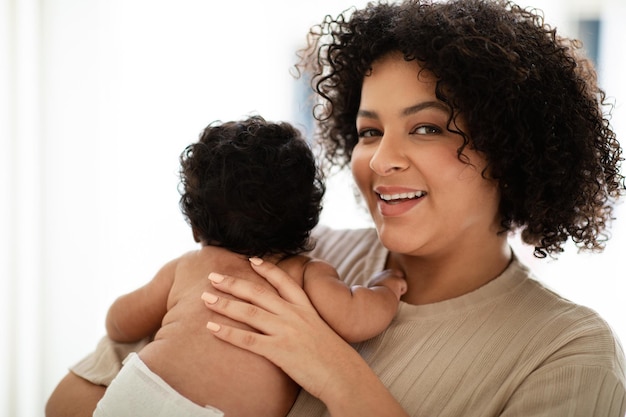 Allegra donna afroamericana millenaria che tiene un bambino piccolo in pannolino gode di cure mediche in camera