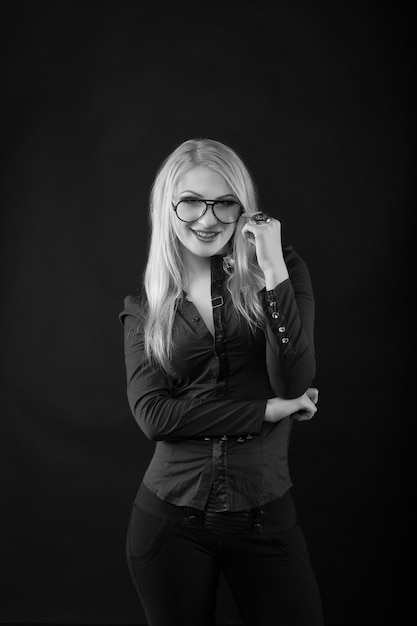 Allegra donna bionda con i capelli lunghi indossa occhiali e camicetta in posa in studio. Scatto in bianco e nero