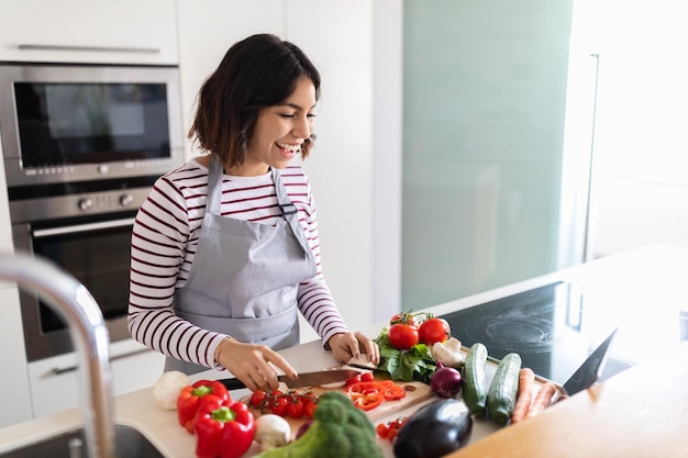 Allegra donna ispanica che si diverte a cucinare a casa utilizzando la tavoletta digitale