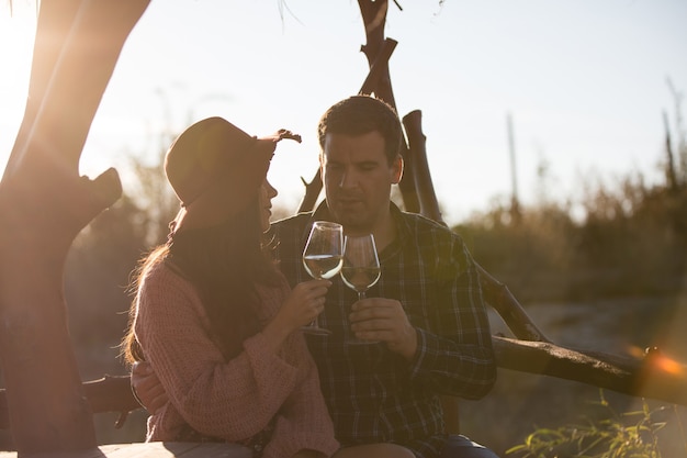 Allegra giovane coppia che ha una conversazione seduta su una panchina in un vigneto tintinnando un bicchiere di vino.