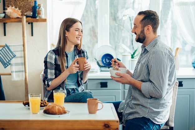 Allegra giovane coppia in abiti casual che sorride e fa colazione a casa