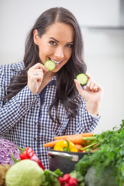 Allegra giovane donna che tiene le fette di cetriolo in cucina - dieta vegetale e concetto di brughiera.