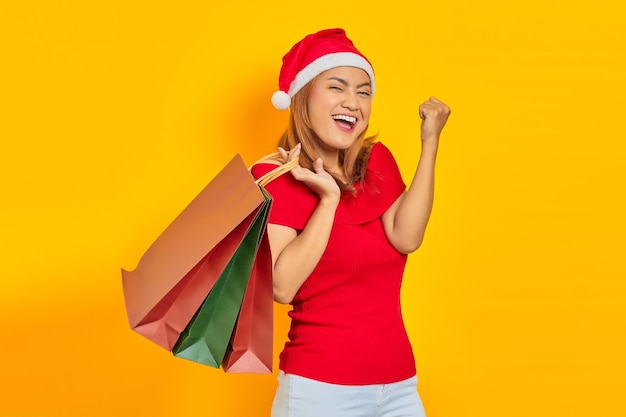 Allegra giovane donna con il cappello di Babbo Natale che tiene in mano le borse della spesa e celebra la soddisfazione dello shopping