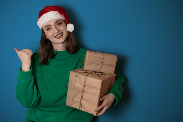 Allegra giovane donna sorpresa indossare maglione natalizio cappello da Babbo Natale in posa puntando le mani braccia a parte indicare sull'area di lavoro isolata su sfondo verde chiaro pastello Happy New Year 2023 concetto di vacanza