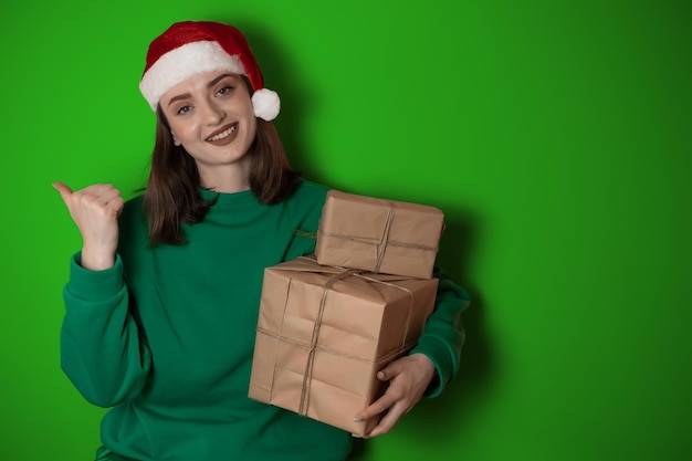 Allegra giovane donna sorpresa indossare maglione natalizio cappello da Babbo Natale in posa puntando le mani braccia a parte indicare sull'area di lavoro isolata su sfondo verde chiaro pastello Happy New Year 2023 concetto di vacanza