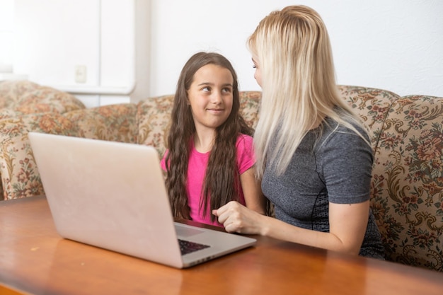 Allegra madre felice sorridente e sorridente e la sua piccola figlia curiosa sono sdraiate su un pavimento a casa e usano un laptop per guardare i cartoni animati, una ragazza sta indicando sul monitor durante il fine settimana.