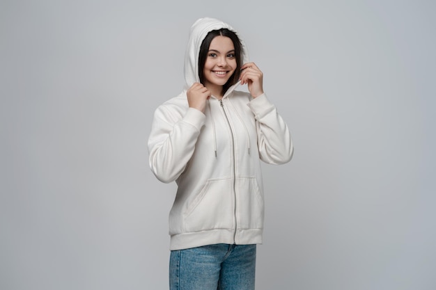 Allegra ragazza adolescente che indossa il cappuccio sulla testa in piedi isolato su sfondo grigio che guarda l'obbiettivo
