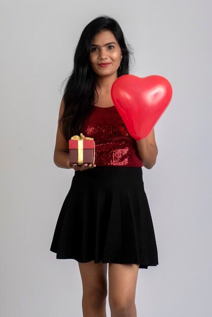 Allegra ragazza carina in abito elegante in posa con palloncino a forma di cuore e confezione regalo.