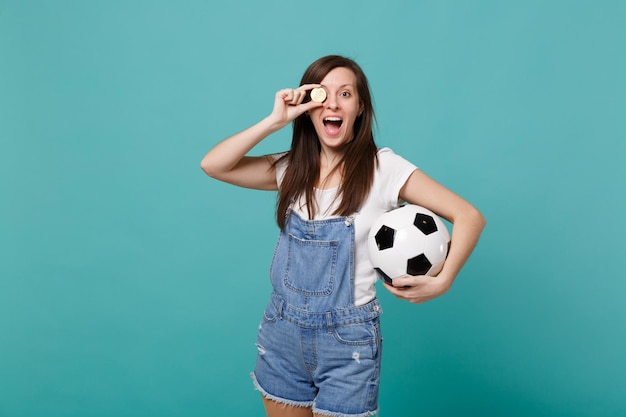 Allegra ragazza fan di calcio supporta la squadra preferita con pallone da calcio, coprendo l'occhio con bitcoin valuta futura isolata su sfondo blu turchese. Emozioni della gente, concetto di svago della famiglia di sport.