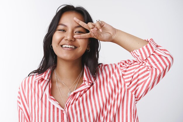 Allegra ragazza sud-asiatica, sorridente spensierata, che mostra vittoria o segno di pace sull'occhio