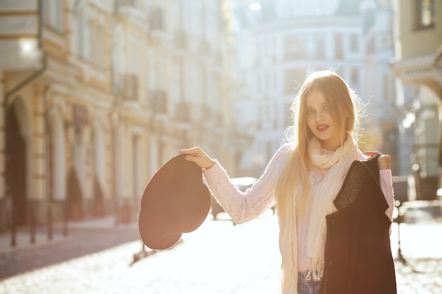 Allegra signora bionda che indossa cappotto e cappello in posa sulla vecchia strada. Spazio per il testo