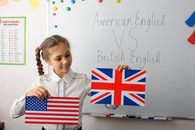 Allegra studentessa con bandiere americane e britanniche in classe, imparando le differenze nei tipi di lingue inglesi
