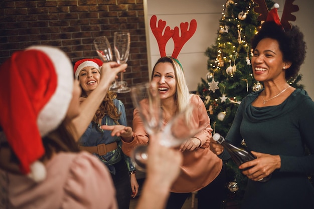 Allegre amiche multietniche che si divertono e fanno un brindisi con champagne mentre festeggiano insieme il nuovo anno o il Natale a casa.