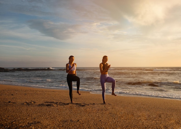 Allegre gemelle caucasiche millenarie le donne fanno esercizi per le gambe correre si divertono ad allenarsi all'aperto sul mare