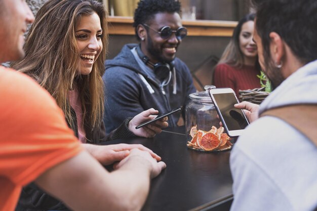 Allegri amici internazionali degli anni '20 si riuniscono al ristorante caffetteria utilizzando gli smartphone mobili