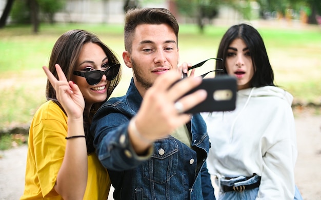 Allegri amici sorridenti al parco seduti su una panchina e scattare selfie utilizzando uno smart phone