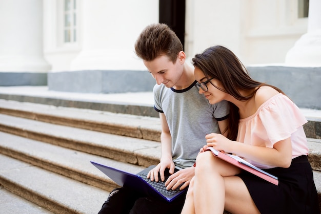 Allegri studenti seduti sulle scale dell'università e facendo insieme progetti per le classi