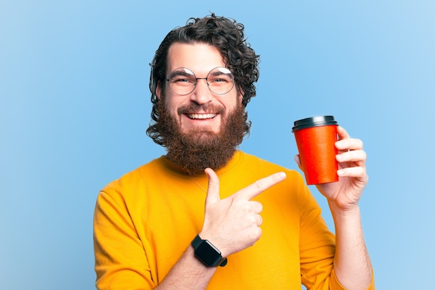 Allegro barbuto hipster uomo che punta alla tazza di caffè da asporto