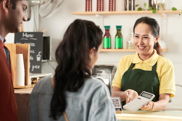 Allegro barista femminile maturo che mostra il prezzo dell'ordine sulla calcolatrice ai clienti