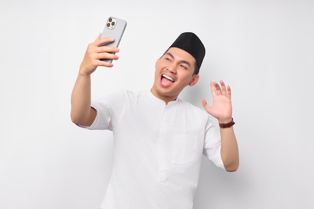 Allegro bel giovane musulmano asiatico in abiti arabi con smartphone che effettua videochiamate o prende selfie isolato su sfondo bianco Concetto di stile di vita islamico religioso della gente