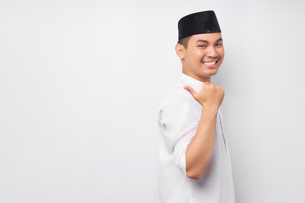 Allegro bel giovane uomo musulmano asiatico che indossa il costume arabo che punta il dito nello spazio libero per un annuncio isolato su sfondo bianco Concetto di stile di vita islamico religioso della gente