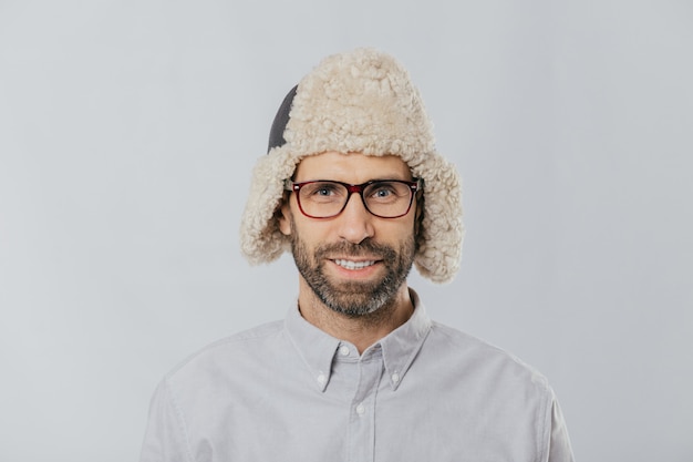 Allegro bel ragazzo indossa un berretto invernale caldo con paraorecchie, occhiali e camicia bianca