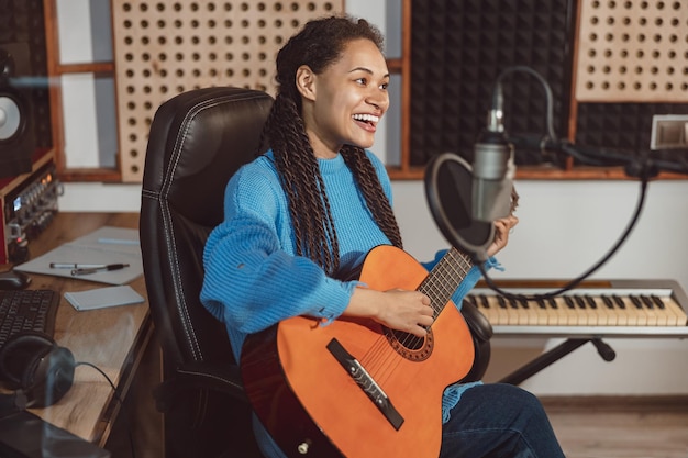 Allegro giovane chitarrista cantante donna africana che suona la chitarra e canta la canzone nel microfono in studio di registrazione del suono