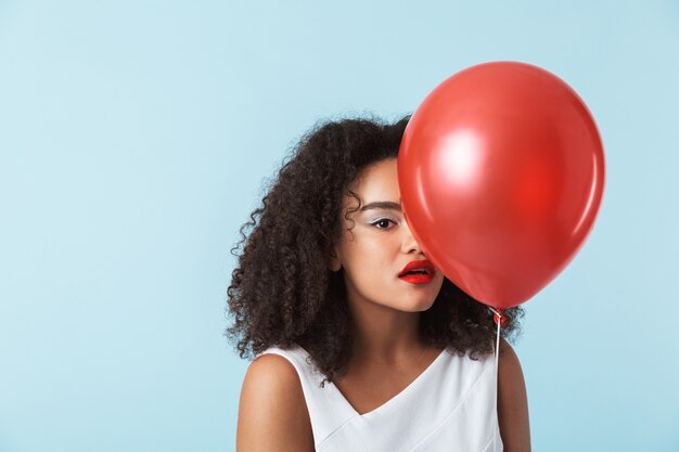 Allegro giovane donna africana che indossa un abito che celebra, tenendo il palloncino isolato