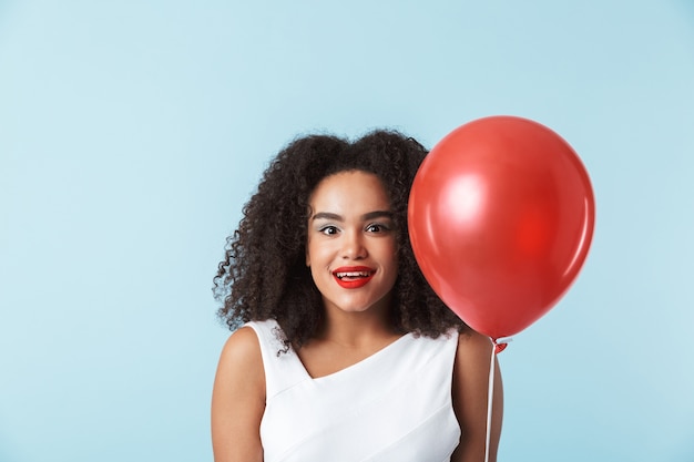 Allegro giovane donna africana che indossa un abito che celebra, tenendo il palloncino isolato