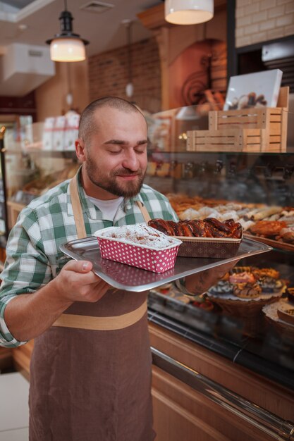 allegro giovane fornaio maschio godendo di lavorare nel suo negozio di panetteria, annusando torte appena sfornate