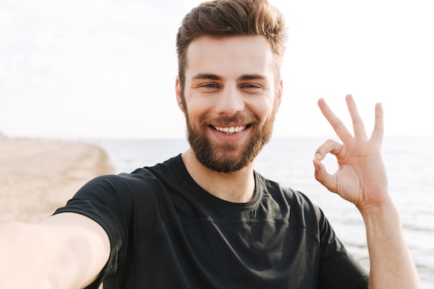 Allegro giovane sportivo con le cuffie che prendono un selfie