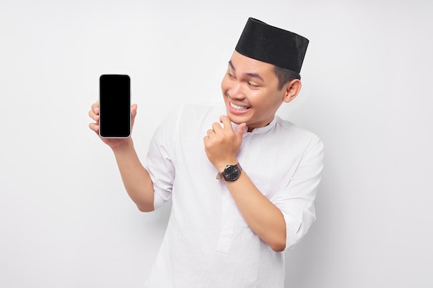 Allegro giovane uomo musulmano asiatico guarda lo schermo dello smartphone toccando il mento pensando all'offerta su sfondo bianco Persone religiose Islam stile di vita concetto celebrazione Ramadan e ied Mubarak