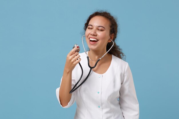 Allegro medico afroamericano donna isolata su sfondo blu ritratto in studio. Medico femminile in abito medico con stetoscopio. Concetto di salute della medicina del personale sanitario. Simula lo spazio della copia.