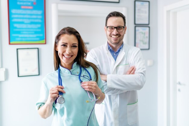 Allegro medico e infermiere in uniforme che propone al corridoio in clinica. Medico con le braccia incrociate. Fuoco selettivo sull'infermiera.